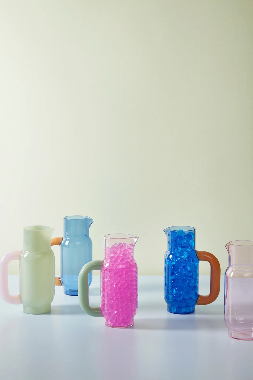 Image 571 - New Trend Row of pastel glass pitchers on a white table, some filled with pink or blue beads.