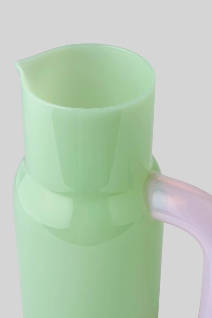 Close-up of a pale green pitcher with a pink translucent handle and narrow pouring spout.