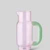 Pink translucent glass pitcher with a mint-green handle on a light gray background, ready for pouring.