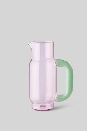 Pink translucent glass pitcher with a mint-green handle on a light gray background, ready for pouring.