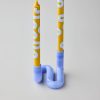Two tall yellow taper candles with white lettering in a glossy blue curved candle holder on a light gray background.
