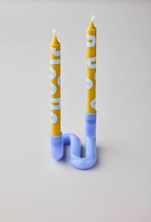 Two tall yellow taper candles with white lettering in a glossy blue curved candle holder on a light gray background.
