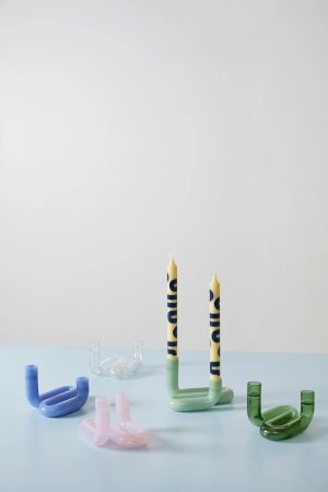 Minimalist still‑life: pastel glass sculptures and two tall blue‑patterned candles on a pale blue surface.