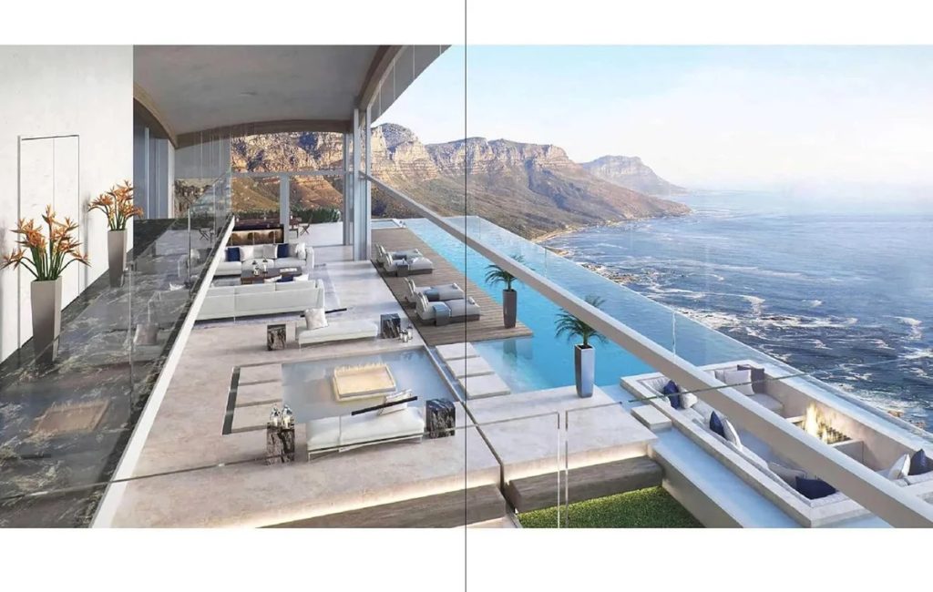 Luxurious glass-walled terrace with white seating, infinity pool, and ocean view overlooking rocky coastline.