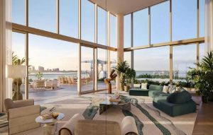 Bright luxury living room with floor-to-ceiling windows, a green sectional, and a water-view cityscape.