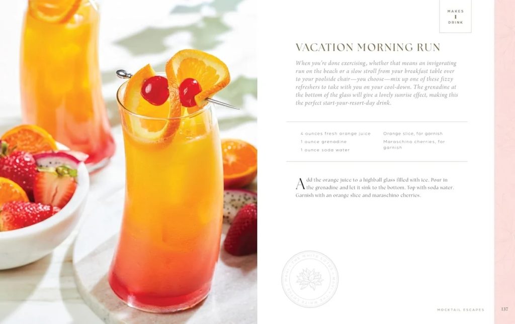 Bright tropical cocktail in a glass with an orange slice and maraschino cherries, gradient orange to pink, with a bowl of strawberries nearby on the left shelf.