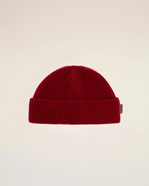 Close-up of a red knit beanie against a pale beige backdrop, showing the top half of the hat.